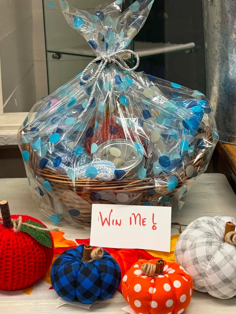 A wrapped gift basket with a Win Me card, surrounded by knitted and fabric pumpkins at Trinity Crafts